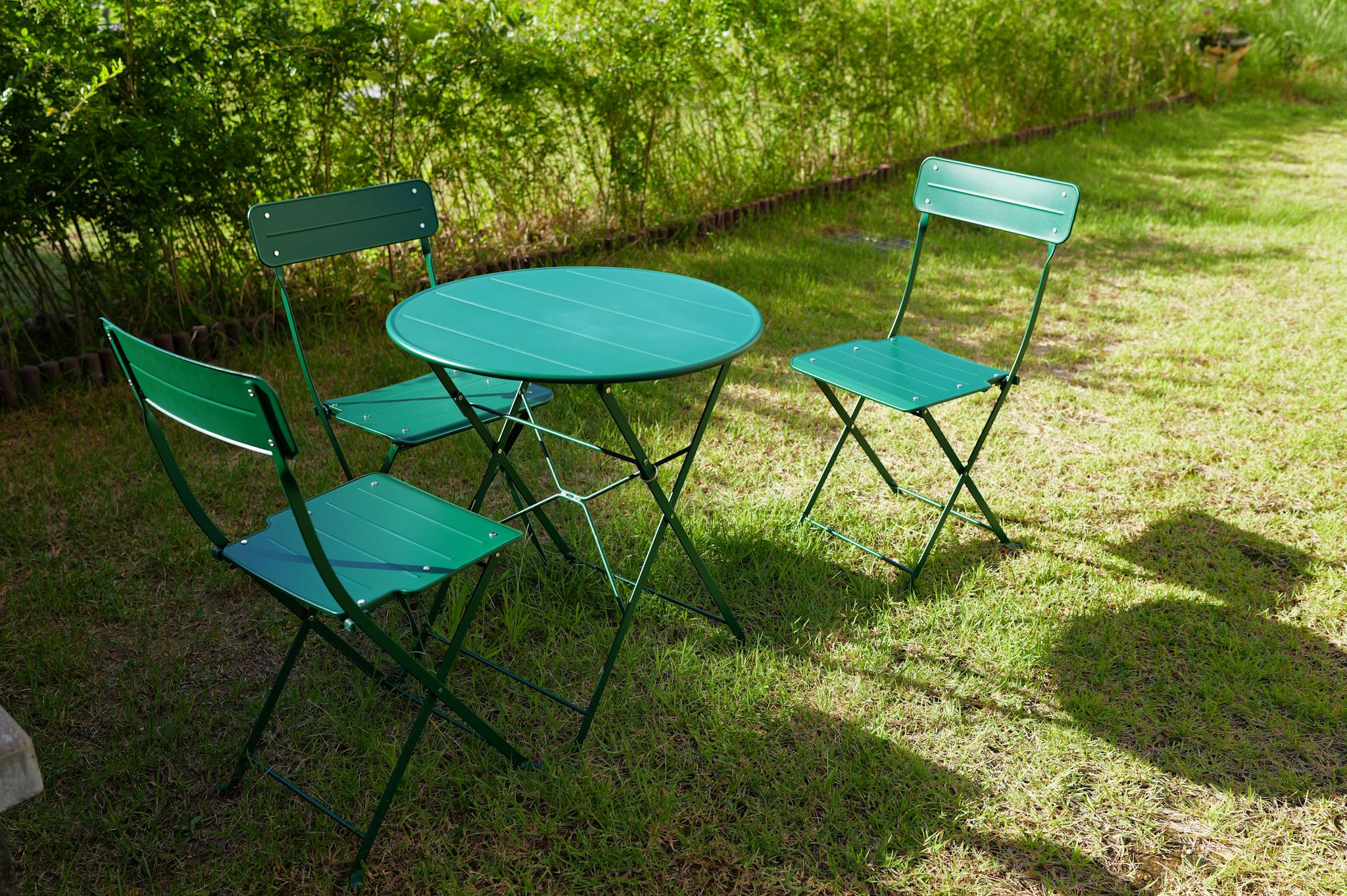 Bistro table and chairs set in a sunny garden with vibrant green surroundings.