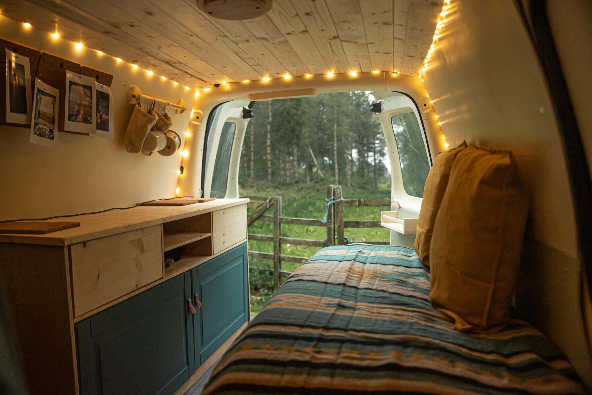 Charming van interior with string lights and forest view, perfect for camping enthusiasts.