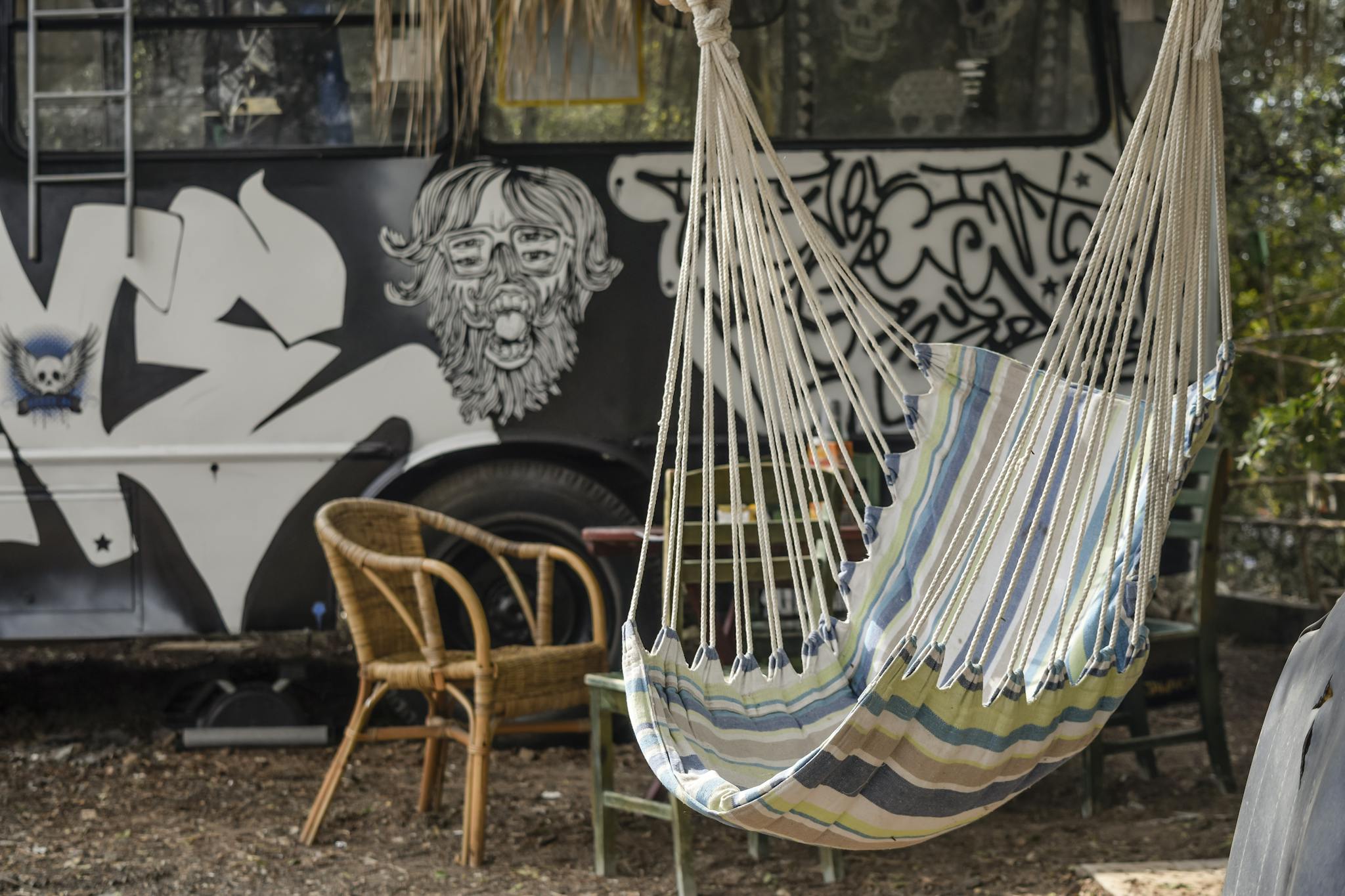 Colorful hammock near a graffiti-covered vehicle with rustic furniture displays a unique outdoor setting.