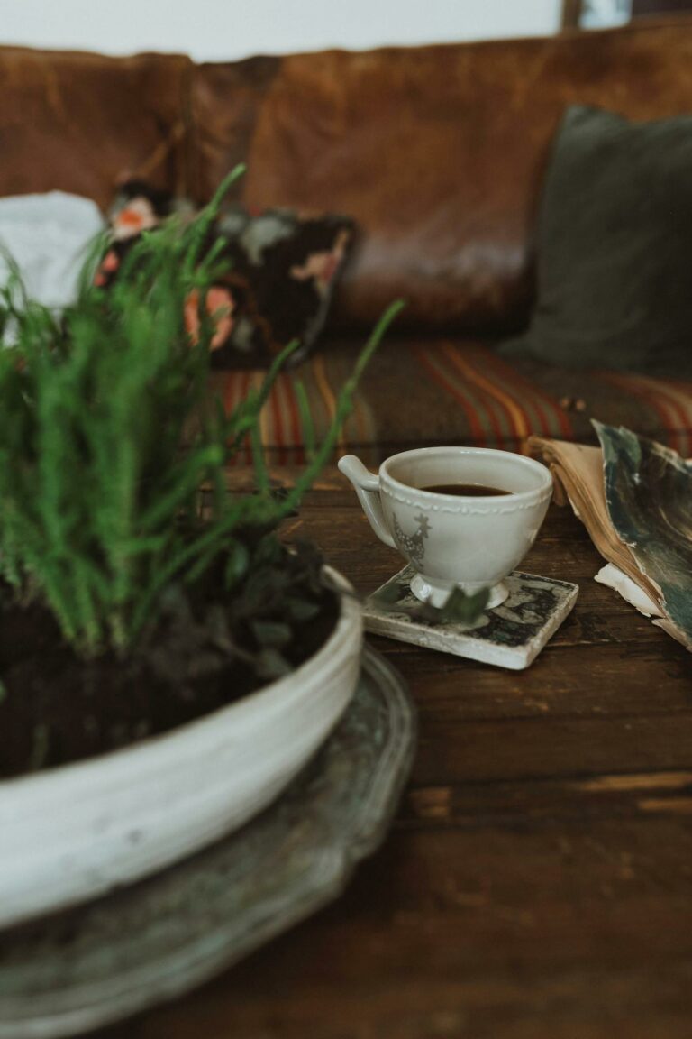 A rustic minimalist setup featuring a cup of coffee with greenery on a wooden table.